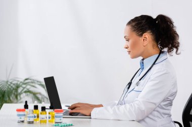 Afro-Amerikan doktorların masadaki esrar ilaçlarının yanında dizüstü bilgisayarda yazışlarının yan görüntüsü
