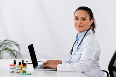 Mutlu Afro-Amerikan doktor masadaki esrar ilaçlarının yanında dizüstü bilgisayarda yazıyor.