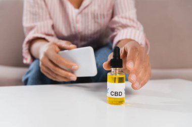 Afro-Amerikalı bir kadının CBC ile şişeye uzanması ve elinde akıllı telefon tutması.