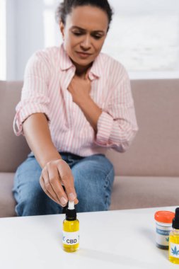 blurred african american woman reaching bottle with cbd letting on table clipart