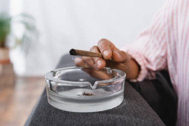 partial view of african american woman holding rolled joint with medical cannabis near ashtray  clipart