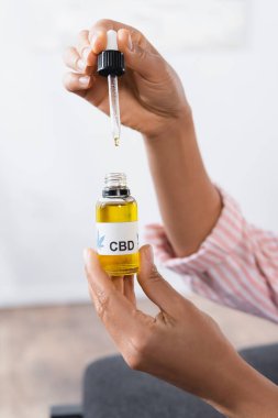 Afro-Amerikan kadının elinde bir şişe dolusu cbd ve pipet vardı. 