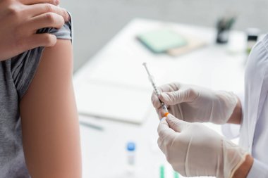 Hastanın koluna yakın bir şırınga tutan doktorun görüntüsü. 