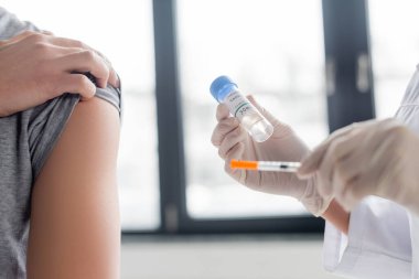 Doktorun yanında aşı ve şırıngayla bulanık ön planda duran adamın görüntüsü. 