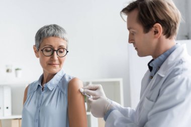 Doctor in latex gloves holding cotton and syringe during vaccination of patient  clipart