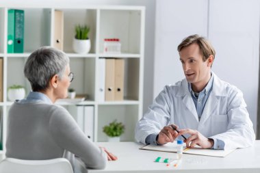 Doktor not defteri ve aşının yanında hastayla konuşuyor.