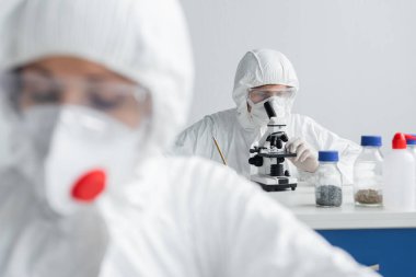 Mikroskop kullanan bilim adamı, meslektaşının yanında bulanık ön plan üzerinde çalışıyor. 