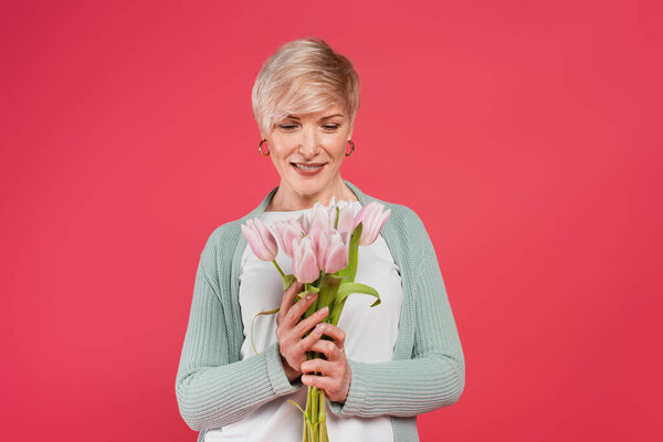 веселая женщина средних лет, держащая свежие тюльпаны изолированы на розовый