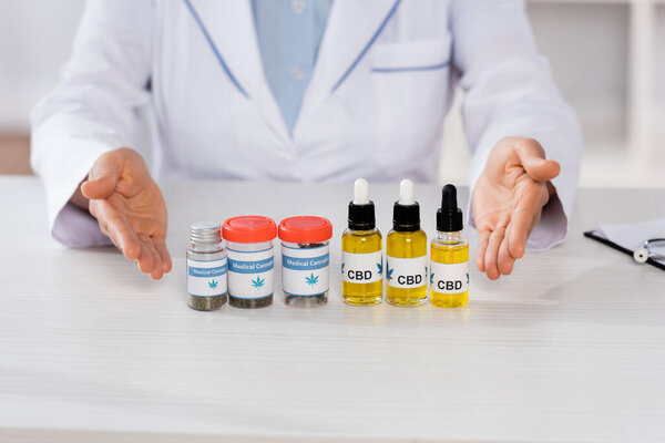 cropped view of african american doctor pointing with hands at bottles with medical cannabis and cbd 
