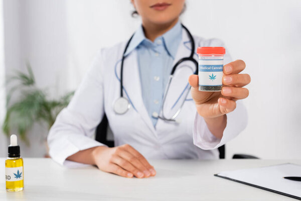 partial view of african american doctor holding bottle with medical cannabis lettering in clinic