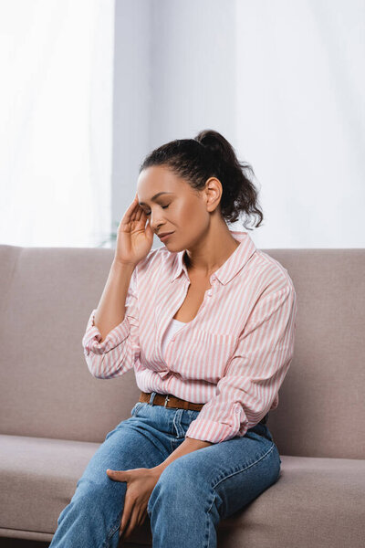 african american woman suffering from headache while sitting on couch 