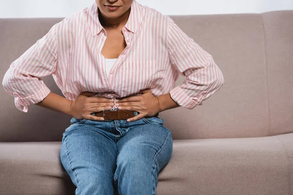 非洲裔美国妇女坐在客厅沙发上肚子痛的剪影 — 图库照片