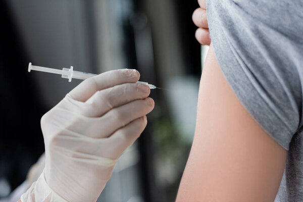 Cropped view of doctor holding syringe near patient during vaccination 
