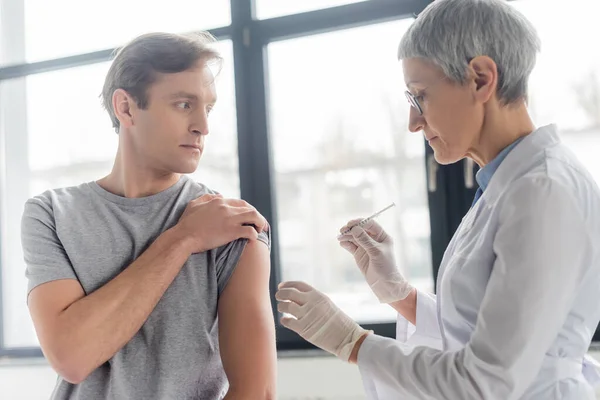 Médecin Mature Manteau Blanc Tenant Seringue Près Homme Clinique — Photo