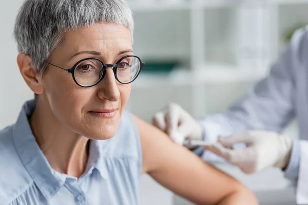 Bulanık Arkaplanda Aşı Sırasında Doktorun Yanında Oturan Olgun Bir Kadın — Stok fotoğraf
