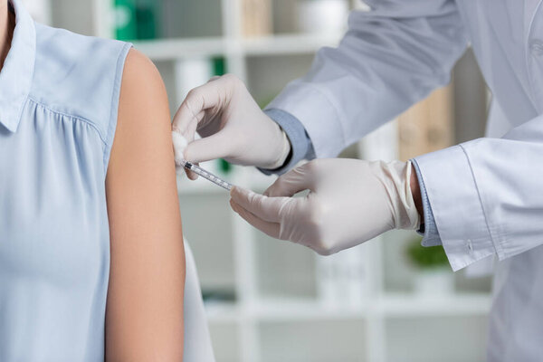 Cropped view of doctor in latex gloves holding syringe and doing vaccination of woman in hospital 