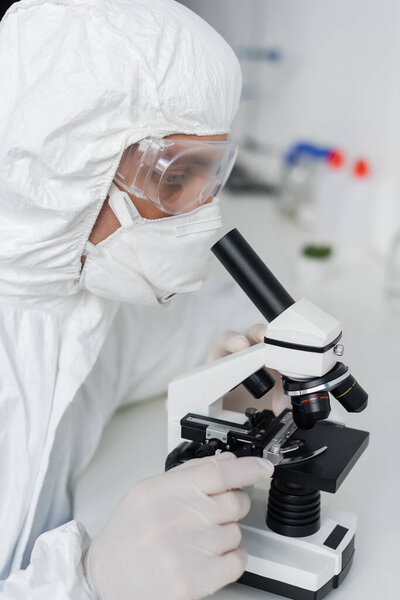 Scientist in latex gloves and goggles using microscope in laboratory 
