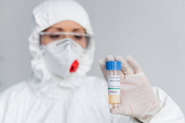 Coronavirus vaccine in hand of scientist in protective uniform blurred on background 