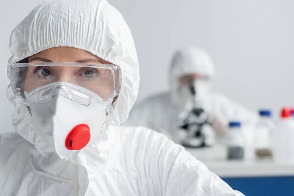 Scientist in goggles and hazmat suit looking at camera in laboratory 