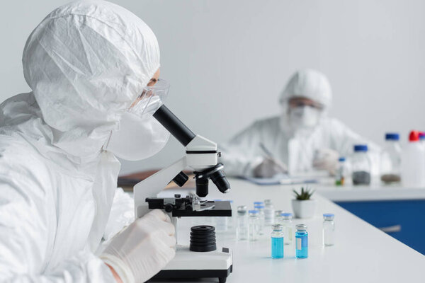 Scientist using microscope near jars with vaccines 