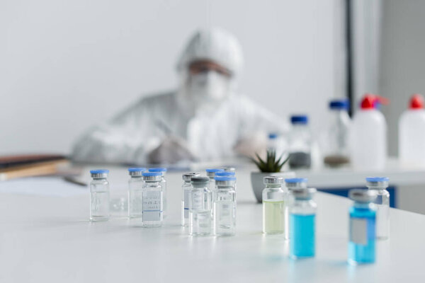 Jars with vaccines near scientist working on blurred background 