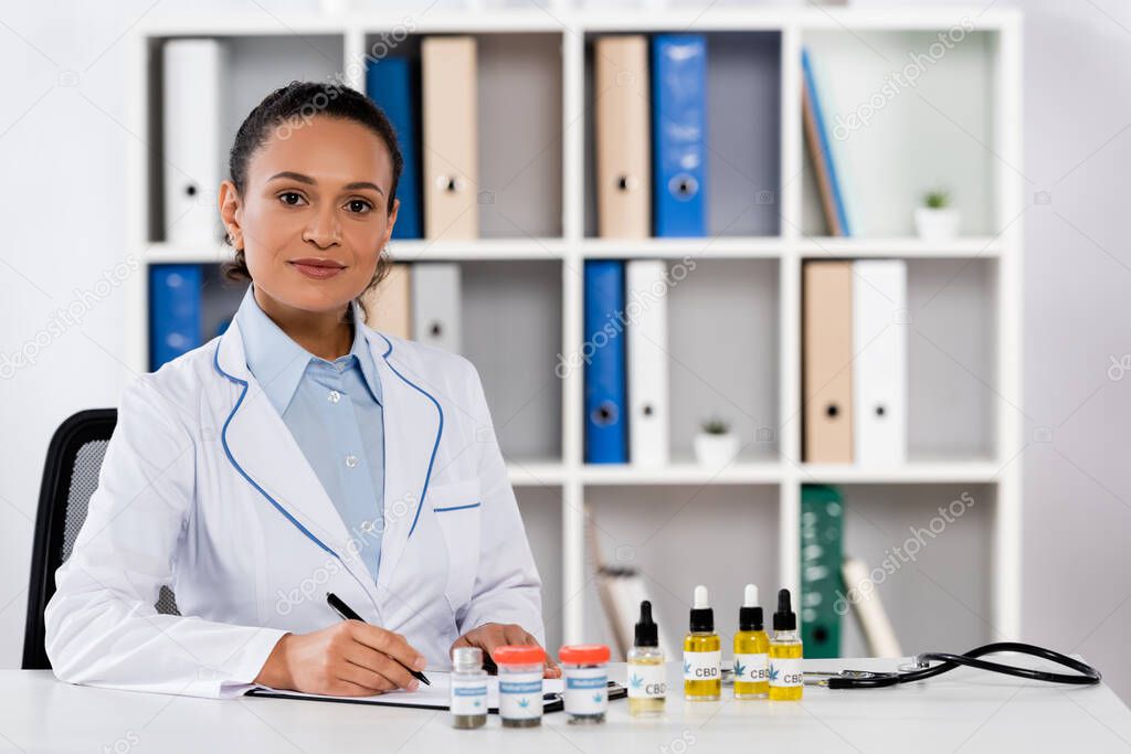 african american doctor writing prescription on clipboard near bottles with legal cbd and medical cannabis 
