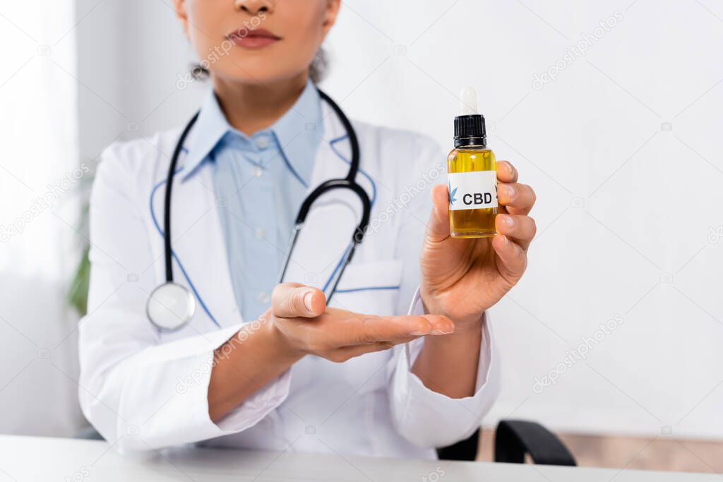 cropped view of african american doctor pointing with hand at bottle with cbd 