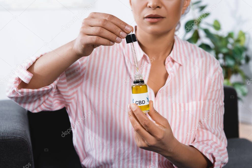 cropped view of african american woman holding bottle with cbd lettering and pipette 