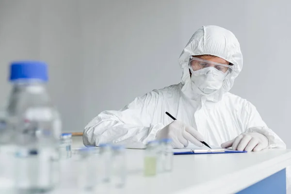 Scientist Writing Clipboard Vaccines Blurred Foreground Table — Stock Photo, Image