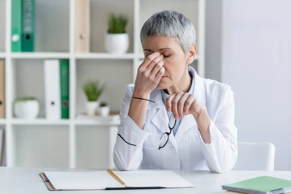 Médico Exausto Segurando Óculos Perto Mesa Trabalho — Fotografia de Stock