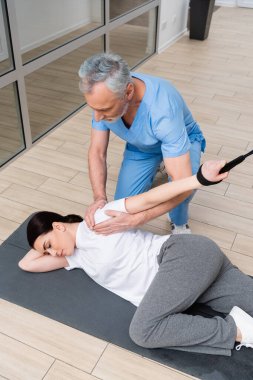 physical therapist helping woman working out on fitness mat in hospital gym clipart