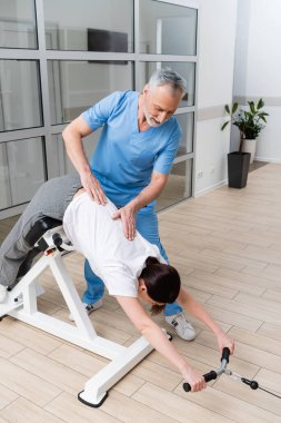 physical therapist supporting woman training in rehabilitation center clipart