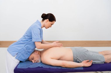 mature man lying on massage table during massotherapy clipart