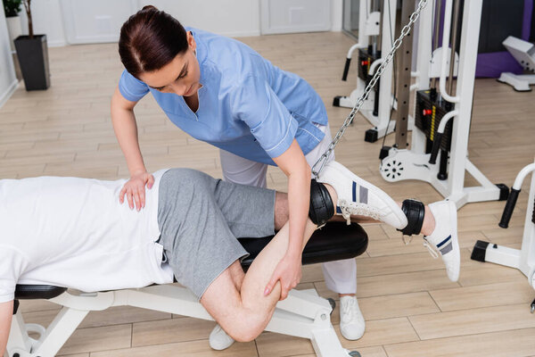 brunette physiotherapist stretching leg of man training in rehabilitation center