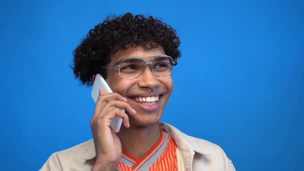 戴眼镜的快乐的非洲裔美国人 用蓝色隔离的智能手机说话 — 图库视频影像