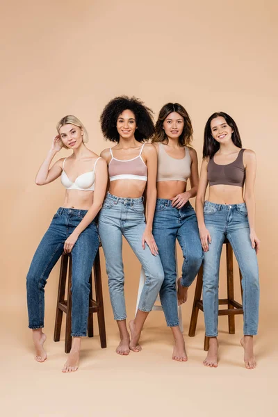 Mujeres Muy Multiétnicas Jeans Sujetadores Posando Cerca Taburetes Altos Beige —  Fotos de Stock
