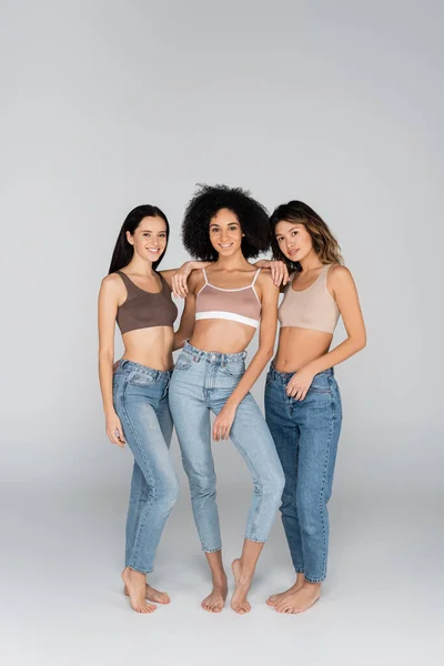 Pretty Multiethnic Women Jeans Bras Looking Camera While Posing Grey — Stock Photo, Image