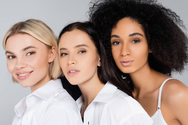 young interracial women with perfect skin looking at camera isolated on grey