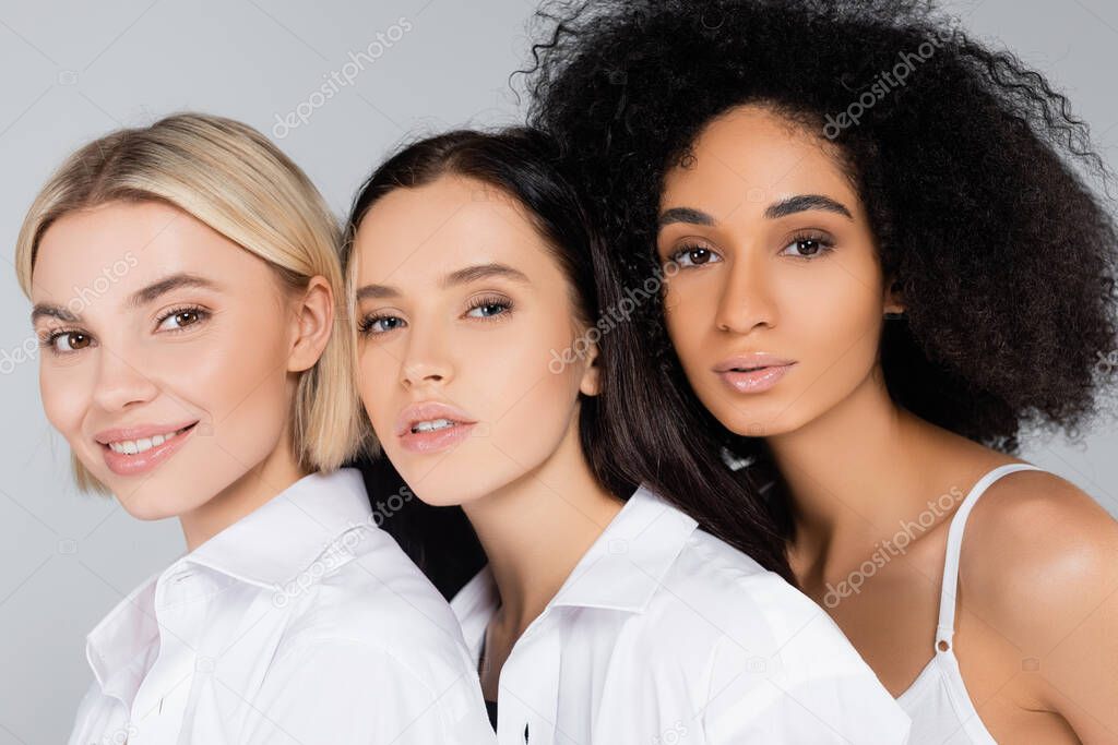 young interracial women with perfect skin looking at camera isolated on grey