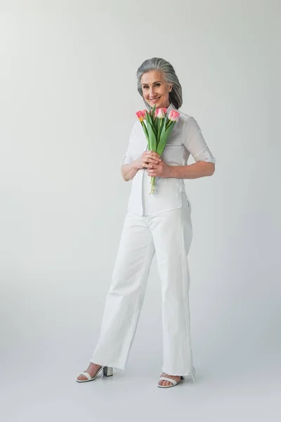 Gammal Kvinna Ler Medan Håller Blommor Grå Bakgrund — Stockfoto