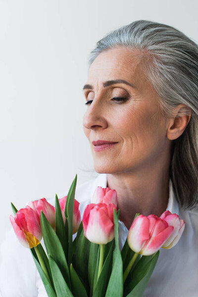 Portrait of mature woman holding tulips isolated on grey 