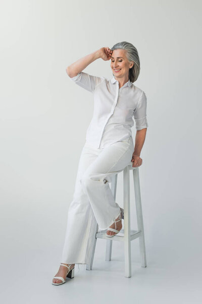 Smiling middle aged woman sitting on chair on grey background 