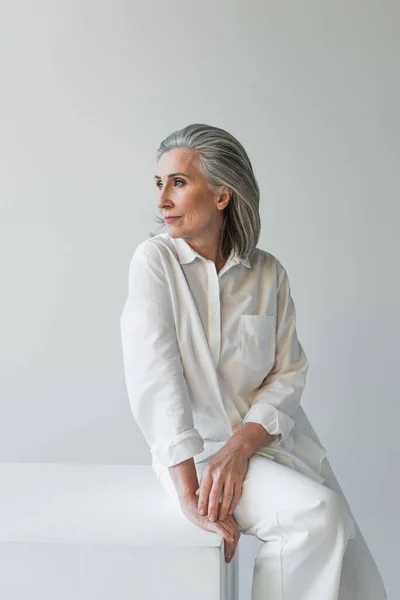 Mature Woman Sitting White Cube Isolated Grey — Stock Photo, Image
