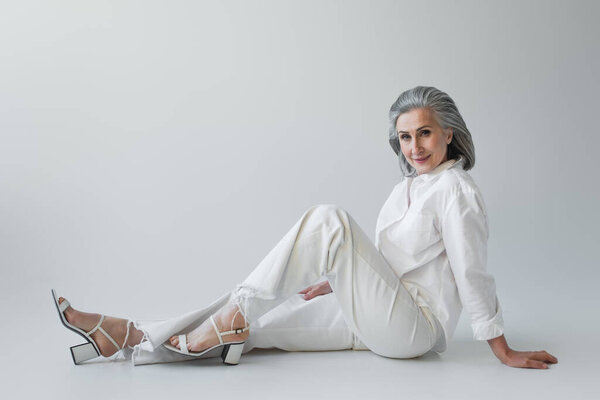 Grey haired woman looking at camera while sitting on grey background 