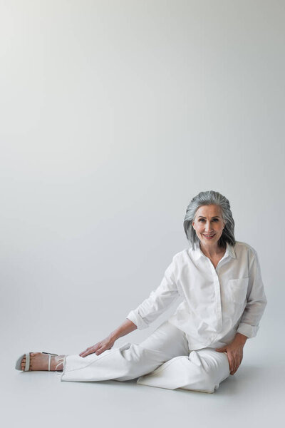 Grey haired woman smiling at camera while sitting on grey background 