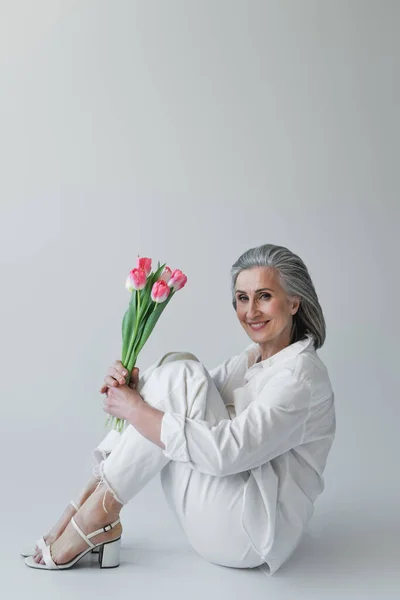 Middle Aged Woman Holding Flowers Smiling Camera While Sitting Grey — Stock Photo, Image