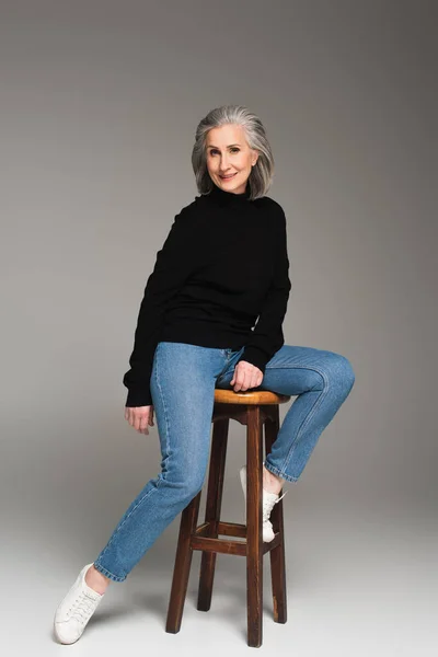 Reife Frau Sitzt Auf Stuhl Und Lächelt Auf Grauem Hintergrund — Stockfoto