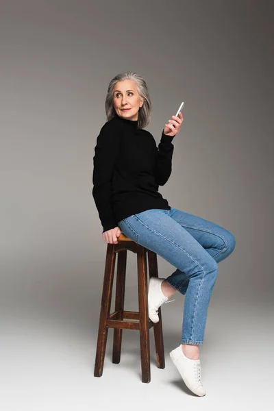 Gammal Kvinna Jeans Håller Smartphone Stol Grå Bakgrund — Stockfoto