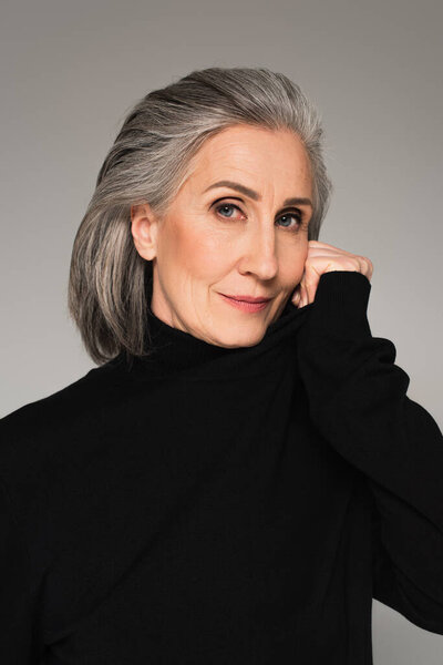 Grey haired woman in black jumper looking at camera isolated on grey 