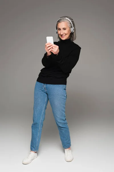 Mulher Sorridente Jeans Jumper Usando Smartphone Fones Ouvido Fundo Cinza — Fotografia de Stock